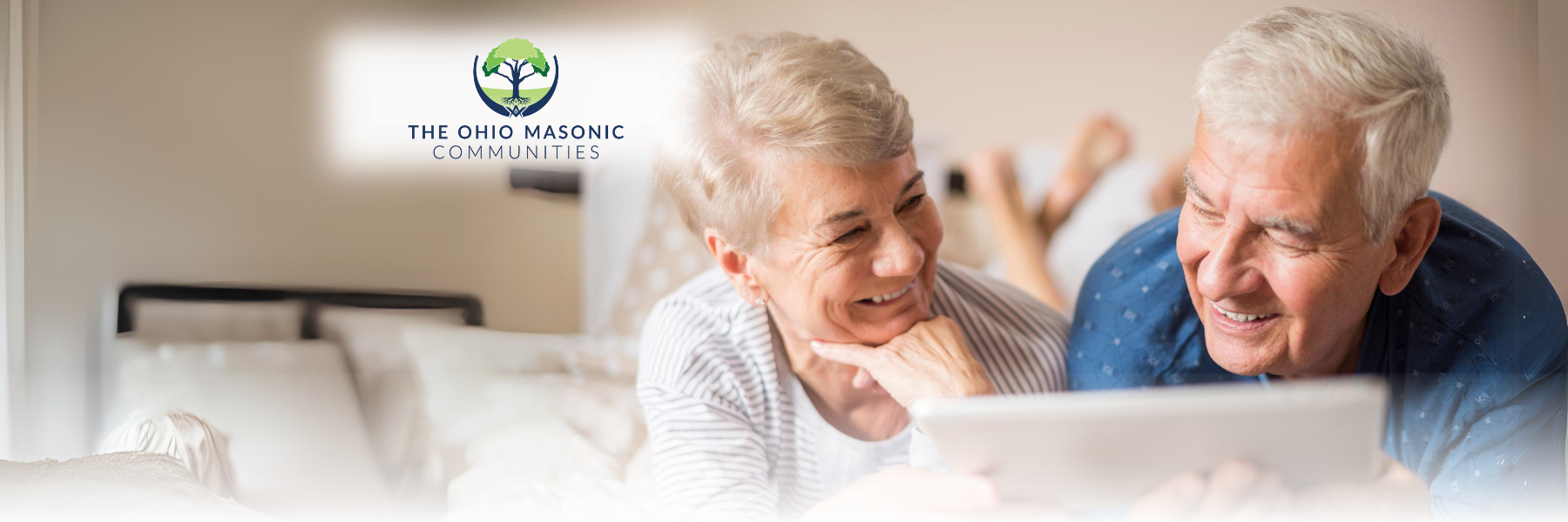 Older adult couple lay on bed and look at a tablet together