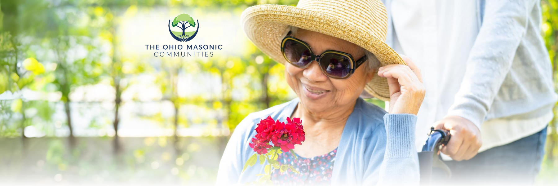 Individual pushes older adult female holding flowers in a wheelchair outside