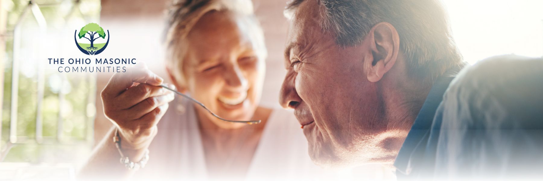 Older adult female playfully feeds an older adult male as they laugh and smile