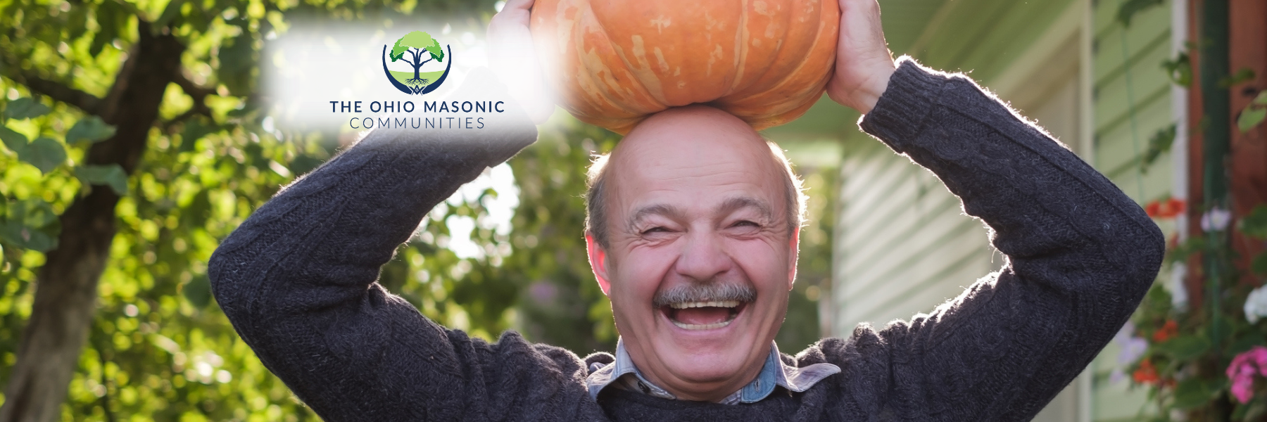 Older adult male holds pumpkin on his head outside