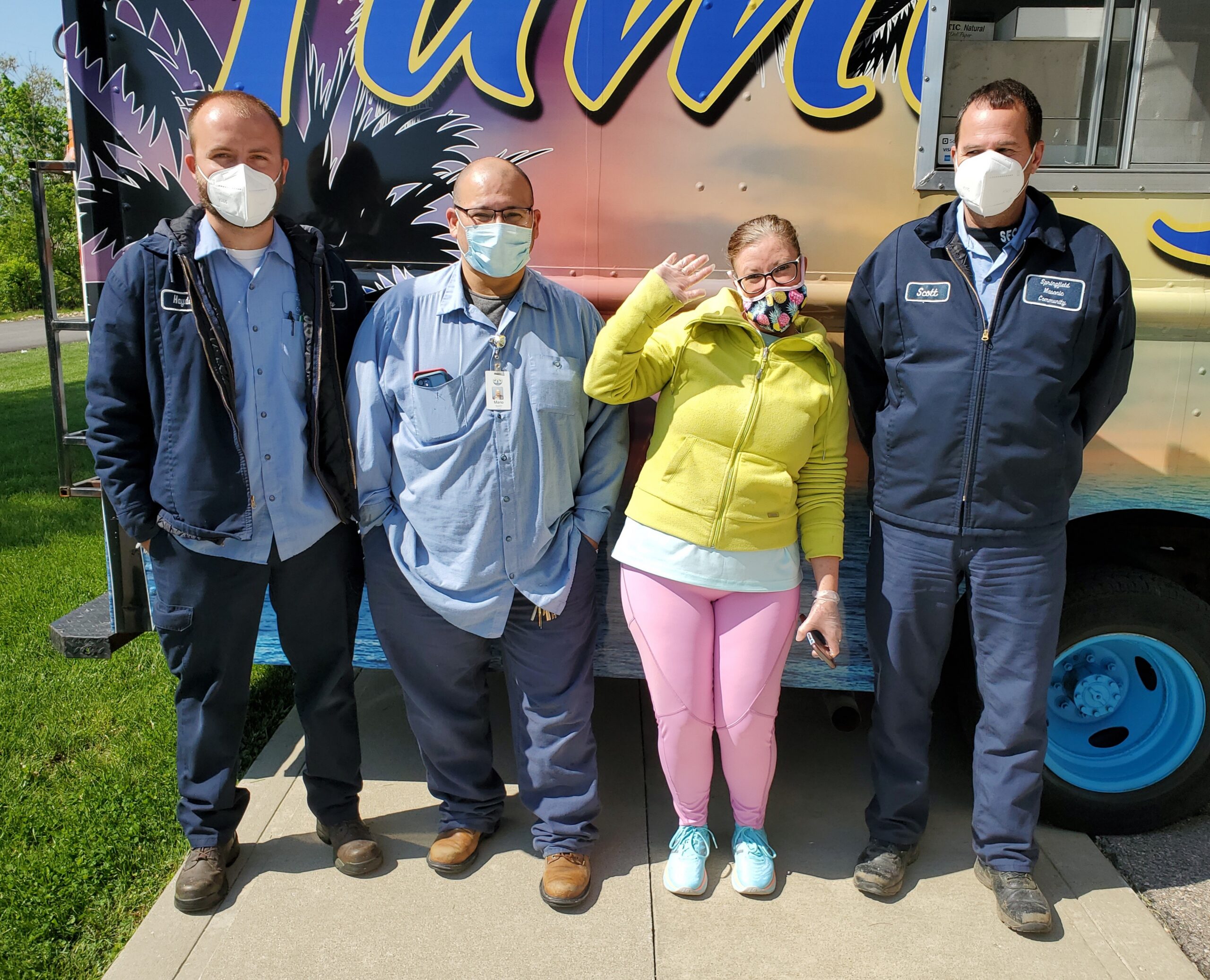 Team members wearing masks pose for a picture outside by the food truck