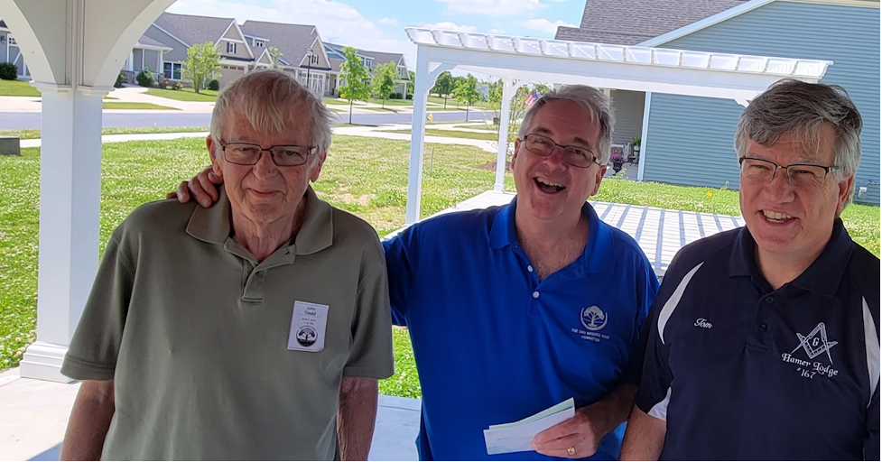 Three older adult males stand together and smile outdoors