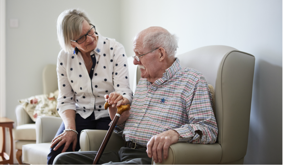 Adult child comforts aging parent that is seated and holding a cane