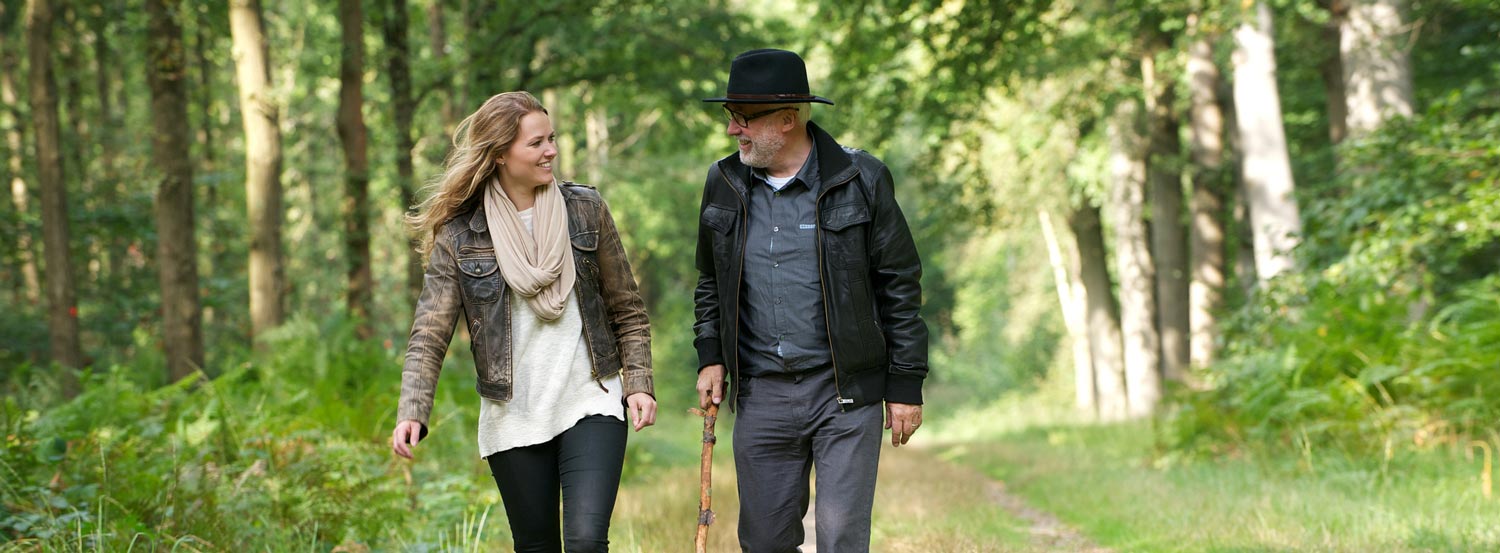 Older adult male walks with cane on a path in the woods with an adult female