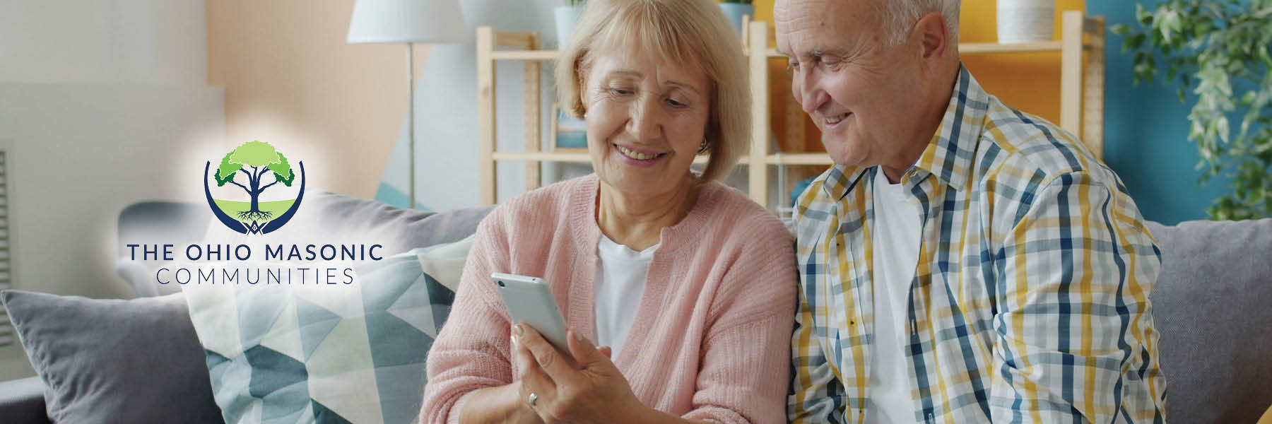 Older adult male and female sitting on a couch and looking at a cell phone