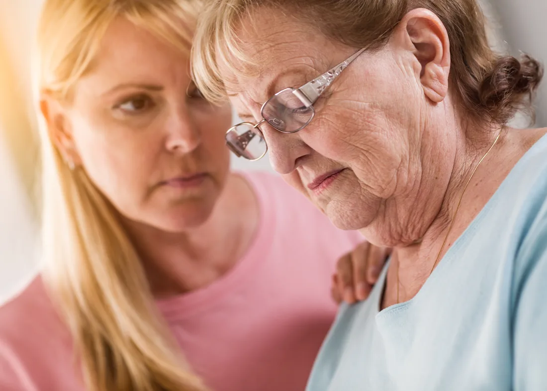 Adult female comforts older adult female by placing a hand on her shoulder