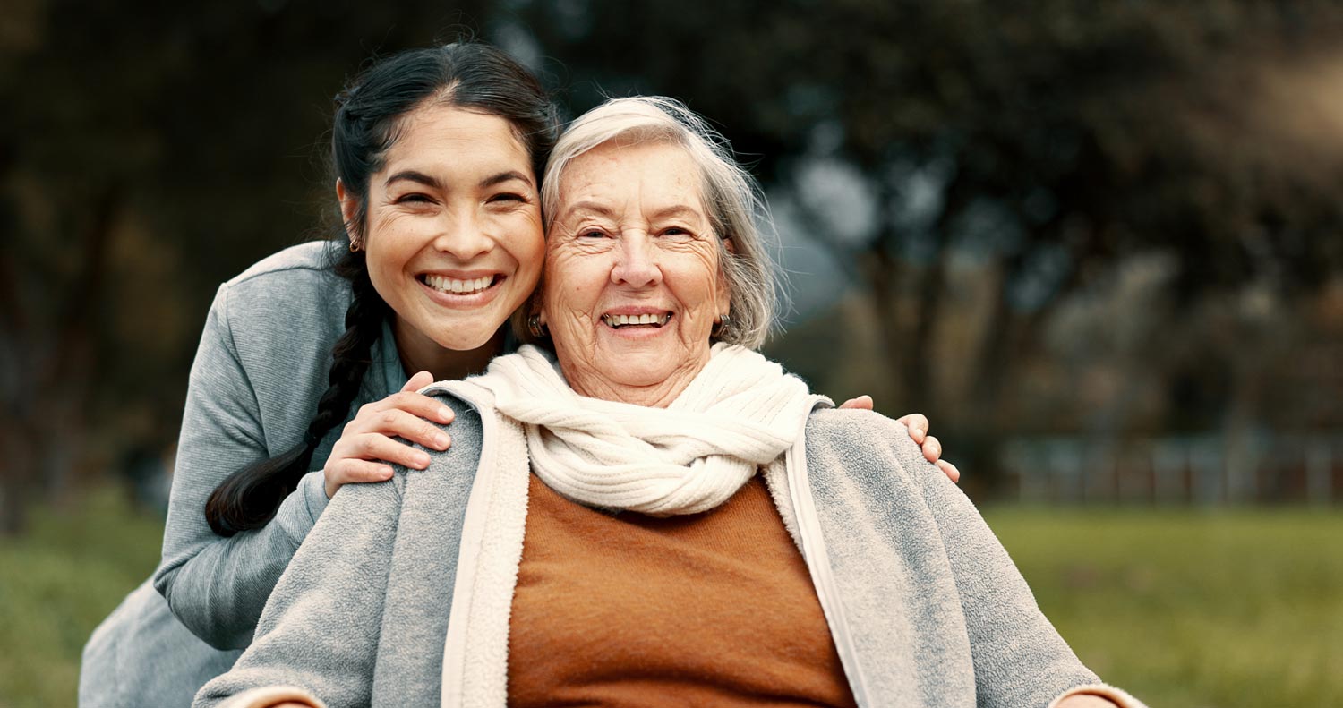 Caregiver embraces older adult female outdoors