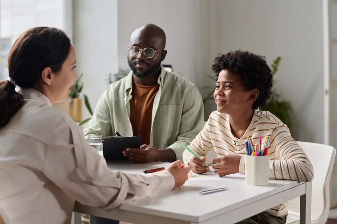 Adult male and young child sit at a table with an adult female