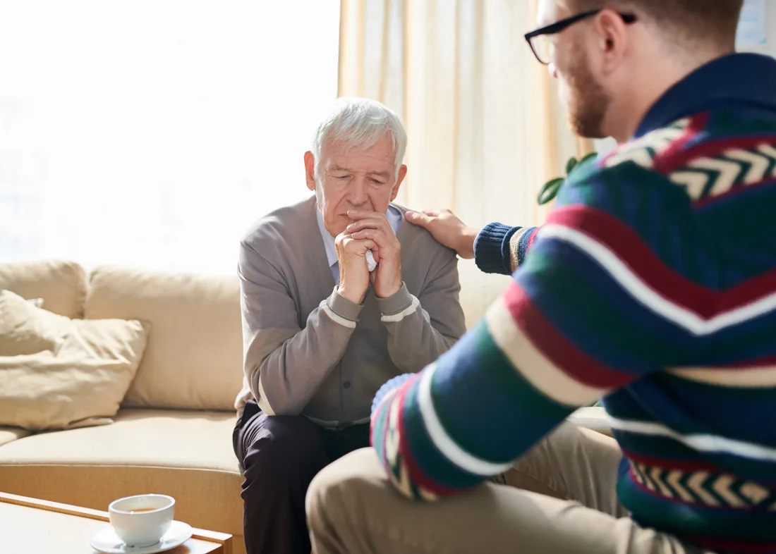 Adult male comforting a male senior who seems distressed