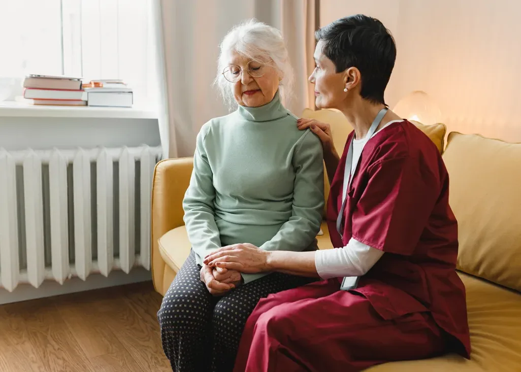Caregiver comforting an older adult female while seated on a couch