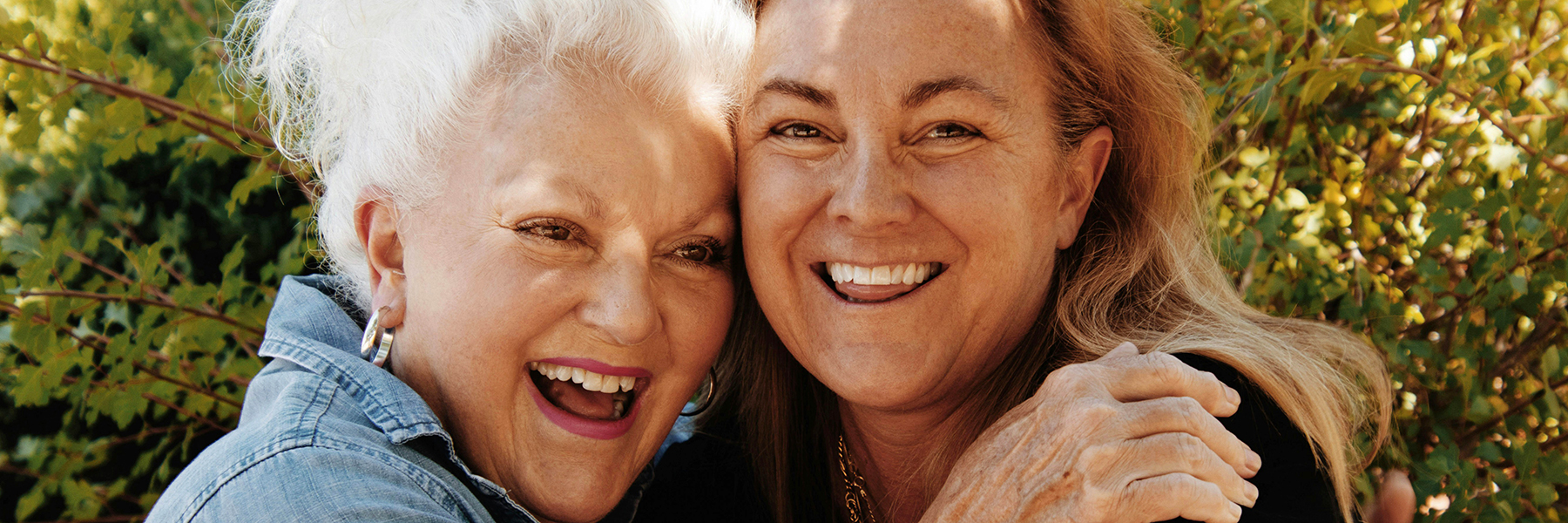 Older adult woman hugs middle aged adult woman as they both laugh outside
